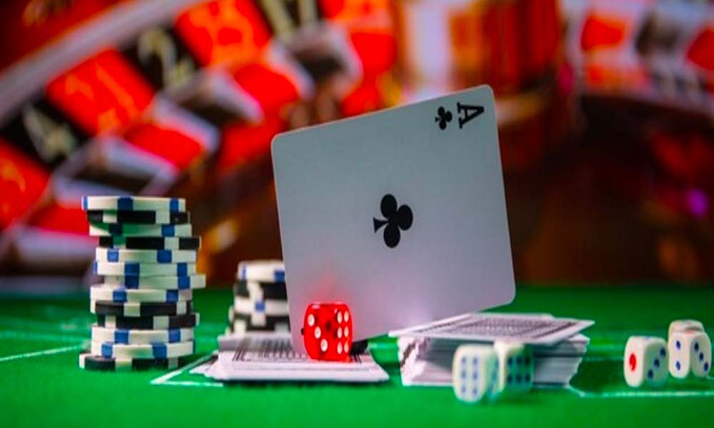 Ett spelkort balanserat på en hög med kasinomarker med tärningar och kort i bakgrunden på ett spelbord på MGA-licenserade casinon.