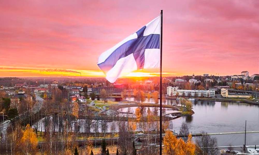 Finsk flagga vajar mot en pulserande solnedgångshimmel över en naturskön stad med höstlöv, som representerar veikkaus mitt i oro för problemspelare.